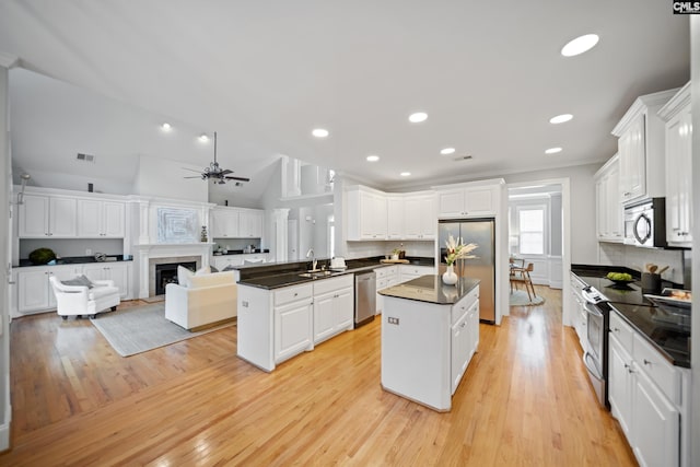 kitchen with a center island, dark countertops, appliances with stainless steel finishes, white cabinetry, and a sink