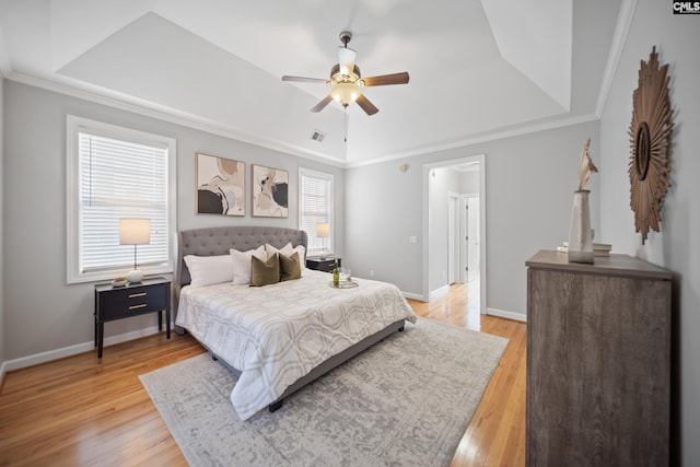 bedroom with light wood-style floors, baseboards, a raised ceiling, and crown molding