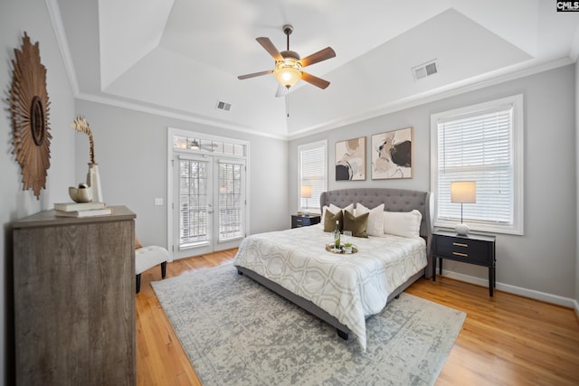 bedroom featuring access to outside, a tray ceiling, light wood-type flooring, and visible vents