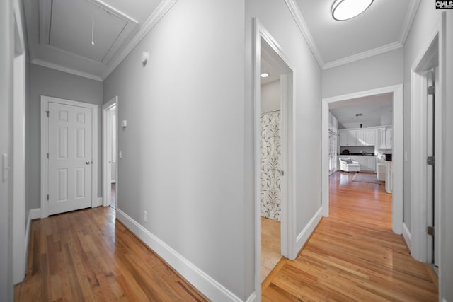 hall with attic access, light wood-style floors, and ornamental molding