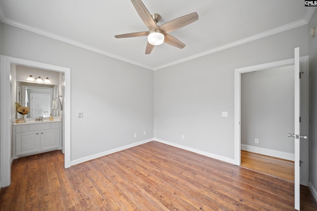 unfurnished bedroom with connected bathroom, a sink, baseboards, hardwood / wood-style floors, and crown molding