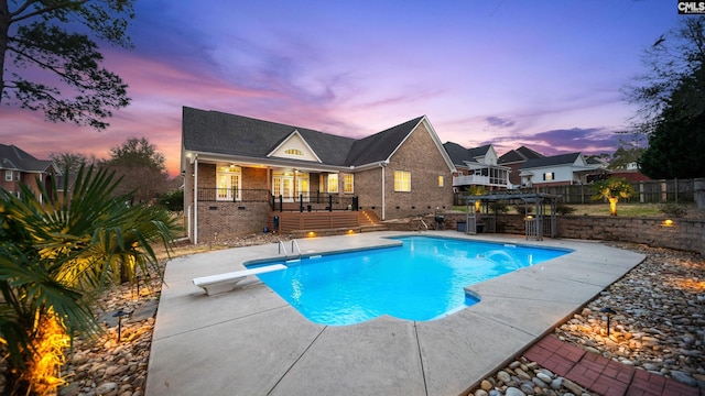 pool at dusk with a diving board, a patio area, fence, and a fenced in pool