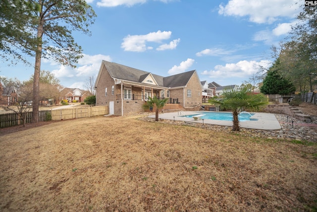 back of house featuring a fenced backyard, a lawn, a fenced in pool, and brick siding