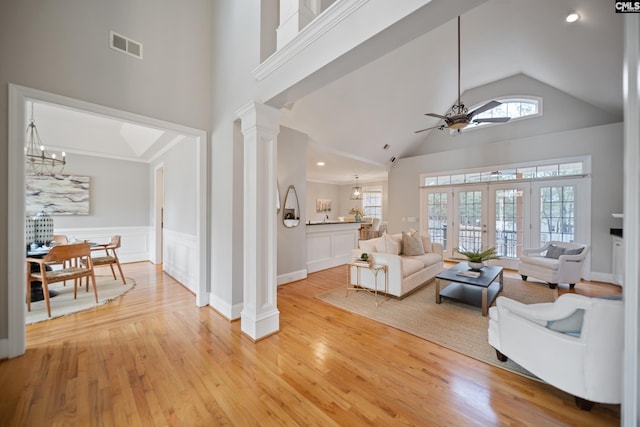 living area featuring visible vents, decorative columns, light wood finished floors, and ceiling fan with notable chandelier