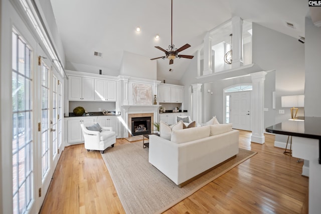 living area featuring light wood-style floors, a wealth of natural light, visible vents, and ornate columns