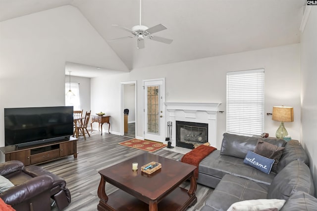 living area with high vaulted ceiling, a fireplace, wood finished floors, a ceiling fan, and baseboards