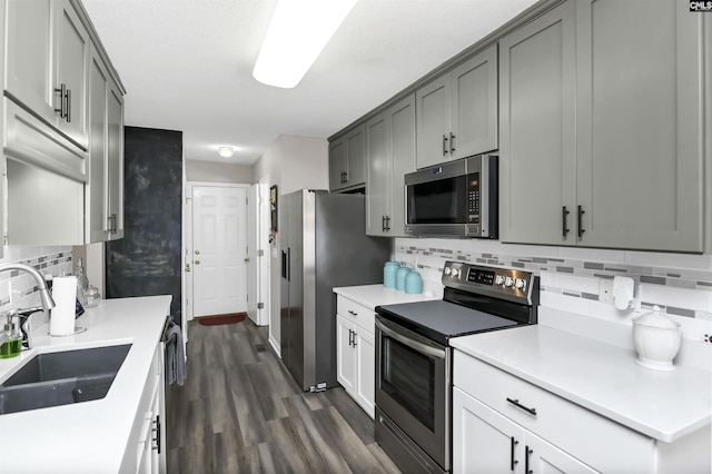 kitchen featuring dark wood-style floors, a sink, stainless steel appliances, light countertops, and backsplash