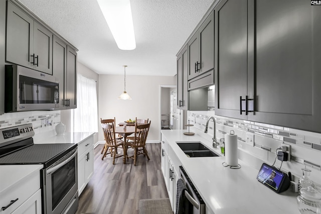 kitchen featuring stainless steel appliances, dark wood-type flooring, a sink, light countertops, and tasteful backsplash