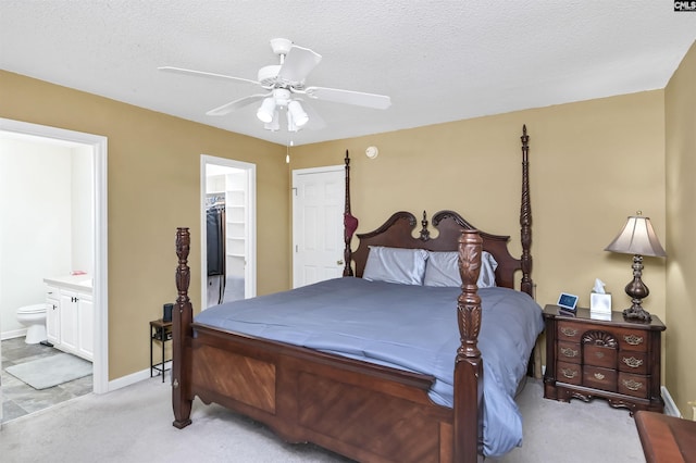 bedroom with ensuite bathroom, ceiling fan, a textured ceiling, light colored carpet, and a walk in closet