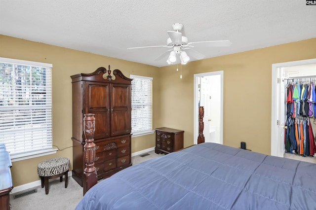 bedroom featuring a walk in closet, light carpet, baseboards, and multiple windows