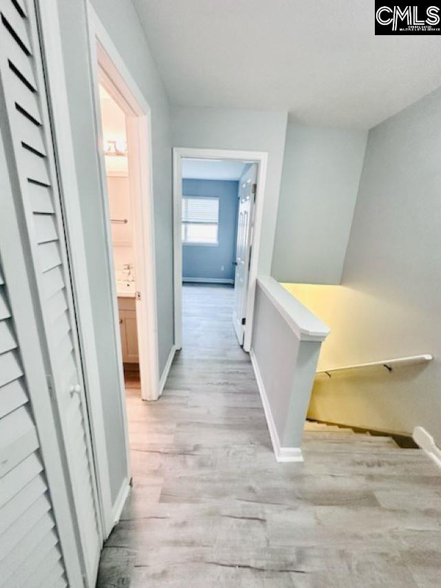 corridor with light wood-type flooring, baseboards, and an upstairs landing