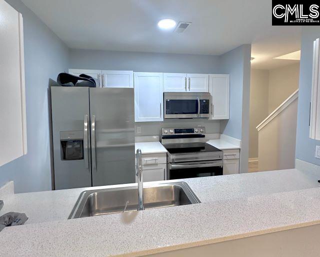 kitchen featuring stainless steel appliances, light countertops, white cabinetry, and a sink