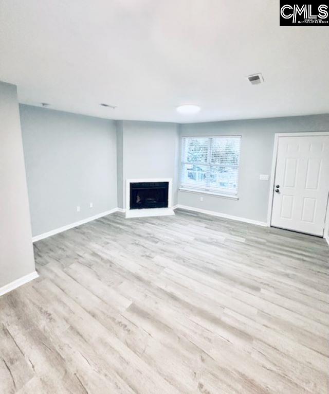 unfurnished living room featuring baseboards, a fireplace, visible vents, and wood finished floors