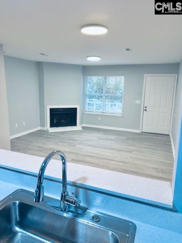 kitchen with a fireplace with raised hearth, wood finished floors, a sink, and baseboards