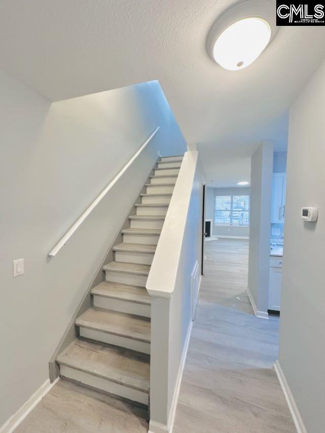 stairway with a textured ceiling, baseboards, and wood finished floors