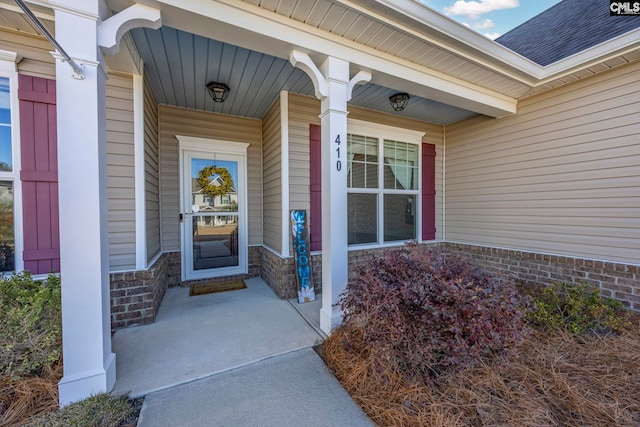 doorway to property featuring stone siding, covered porch, and roof with shingles