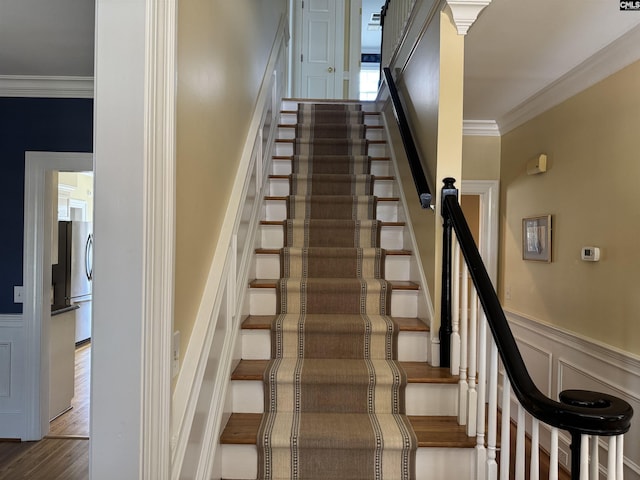 stairway with a decorative wall, wainscoting, wood finished floors, and crown molding