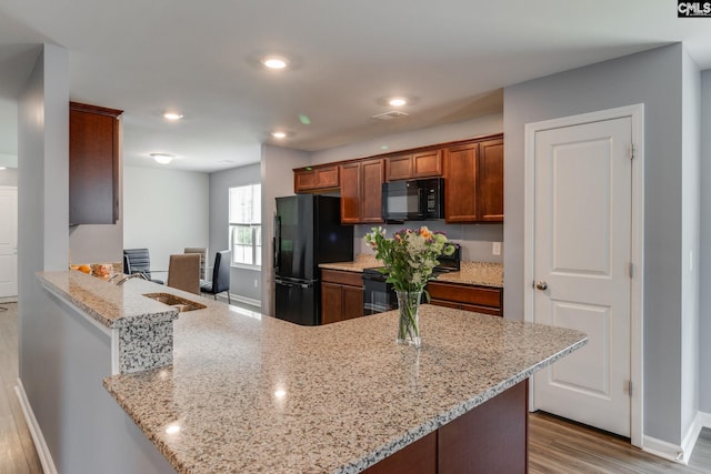 kitchen with light stone counters, recessed lighting, wood finished floors, a sink, and black appliances