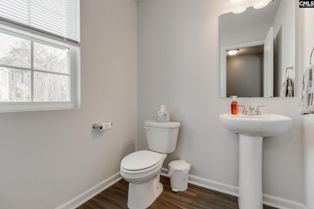 half bathroom with baseboards, toilet, and wood finished floors