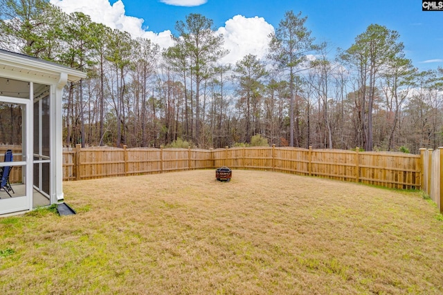 view of yard featuring a sunroom, a fenced backyard, and a fire pit