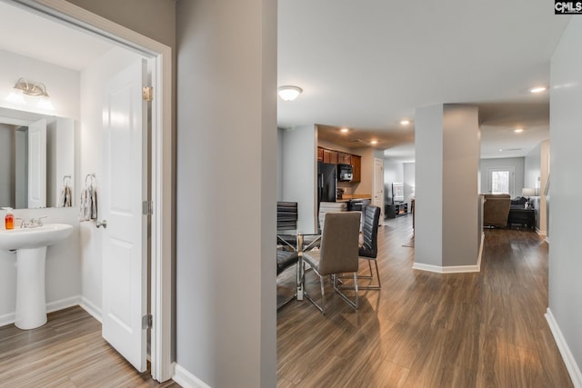 hall featuring a sink, baseboards, dark wood-style flooring, and recessed lighting