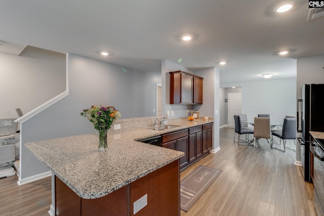 kitchen with light wood-style flooring, a sink, a peninsula, and light stone counters