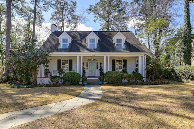 cape cod-style house featuring a porch, a chimney, a front yard, and stucco siding