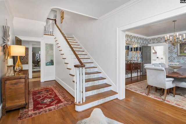 stairway featuring ornamental molding, wood finished floors, a chandelier, and wallpapered walls