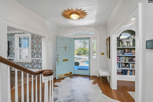 foyer entrance featuring wallpapered walls, crown molding, stairway, and wood finished floors