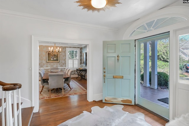 foyer entrance featuring baseboards, crown molding, a chandelier, and wood finished floors