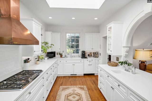 kitchen with a skylight, stainless steel gas cooktop, light wood-style floors, a sink, and ventilation hood