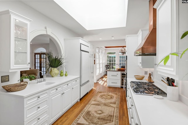 kitchen with glass insert cabinets, light wood-type flooring, white cabinets, and wall chimney range hood