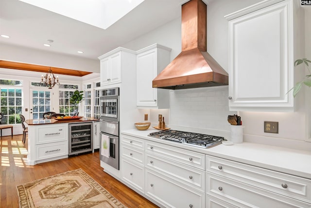 kitchen with light wood-type flooring, beverage cooler, stainless steel gas cooktop, and extractor fan