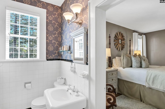 half bath with a wainscoted wall, a sink, tile walls, and wallpapered walls