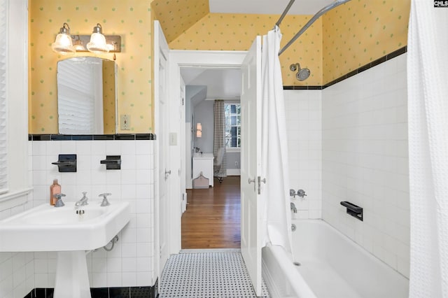 bathroom featuring tile walls, wainscoting, tile patterned floors, shower / bath combo with shower curtain, and wallpapered walls