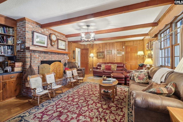 living area featuring a chandelier, a textured ceiling, a fireplace, wood finished floors, and beamed ceiling