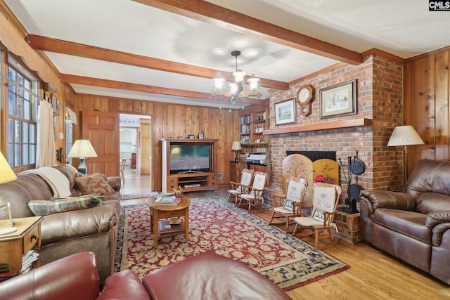 living area featuring wooden walls, a notable chandelier, a fireplace, wood finished floors, and beam ceiling