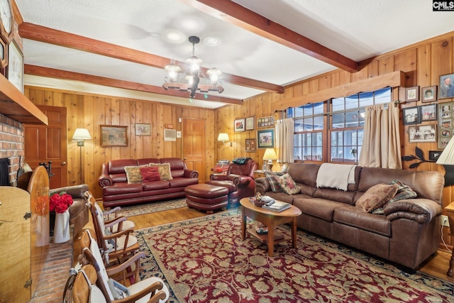 living room with wooden walls, a textured ceiling, wood finished floors, a chandelier, and beamed ceiling