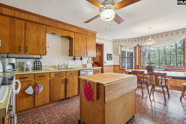 kitchen featuring a wainscoted wall, stainless steel dishwasher, a sink, and wallpapered walls