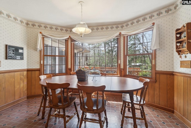 dining room with dark tile patterned flooring, wainscoting, wood walls, and wallpapered walls