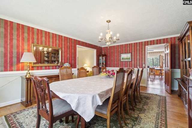 dining area with wallpapered walls, light wood-style flooring, crown molding, and a notable chandelier