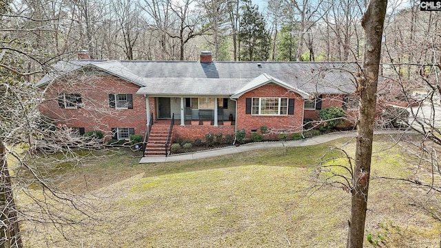 view of front of property featuring a front yard, a chimney, a porch, and brick siding