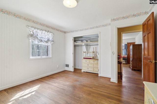 unfurnished bedroom featuring visible vents, a closet, baseboards, and wood finished floors