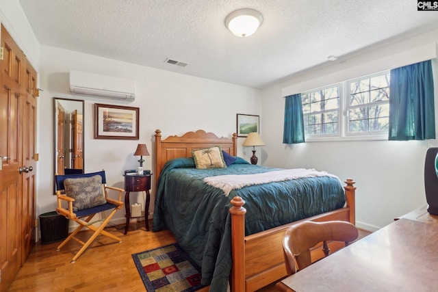 bedroom with visible vents, a textured ceiling, light wood-type flooring, a wall mounted air conditioner, and baseboards