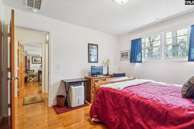 bedroom with a wall unit AC, a textured ceiling, and wood finished floors