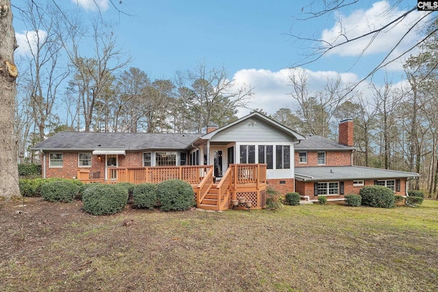 back of property featuring brick siding, a chimney, a lawn, a sunroom, and a deck