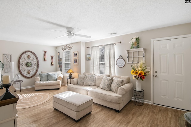 living room featuring a ceiling fan, visible vents, a textured ceiling, and light wood finished floors