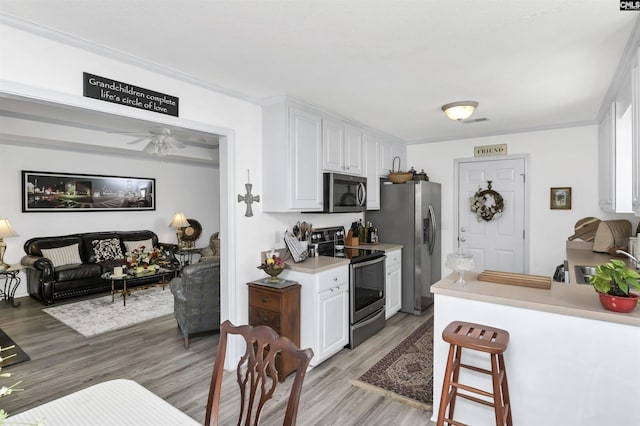 kitchen featuring light wood-style flooring, white cabinets, light countertops, ornamental molding, and appliances with stainless steel finishes