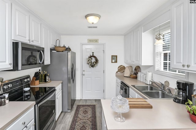 kitchen with light countertops, appliances with stainless steel finishes, a sink, and white cabinets