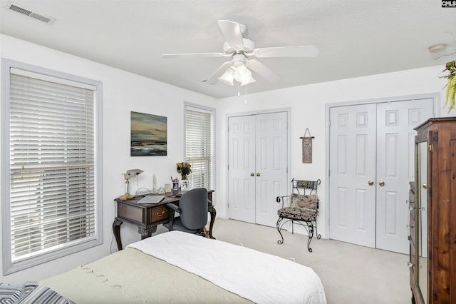 bedroom featuring light colored carpet, visible vents, ceiling fan, and two closets